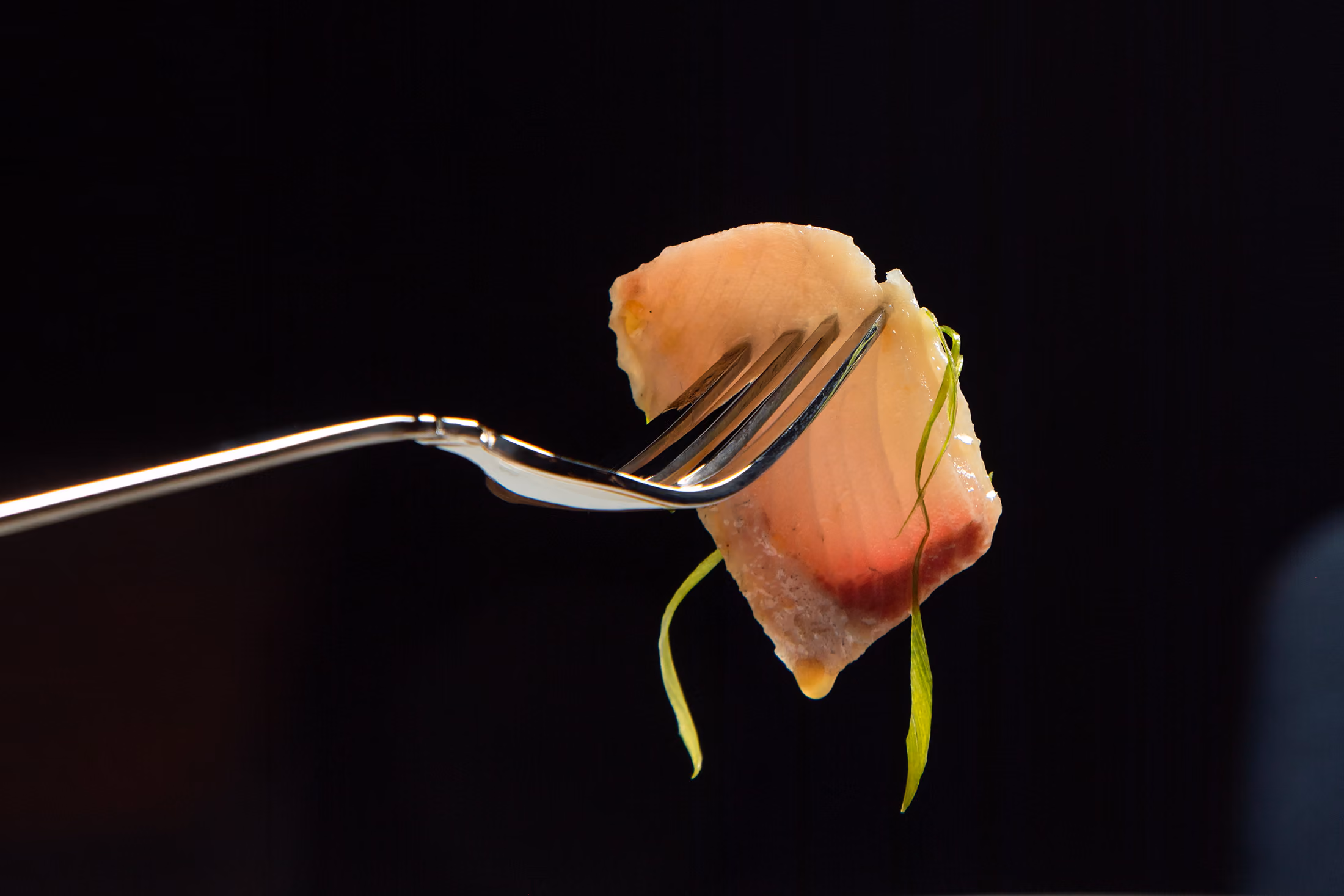 A slice of hamachi crudo lifted on a fork
