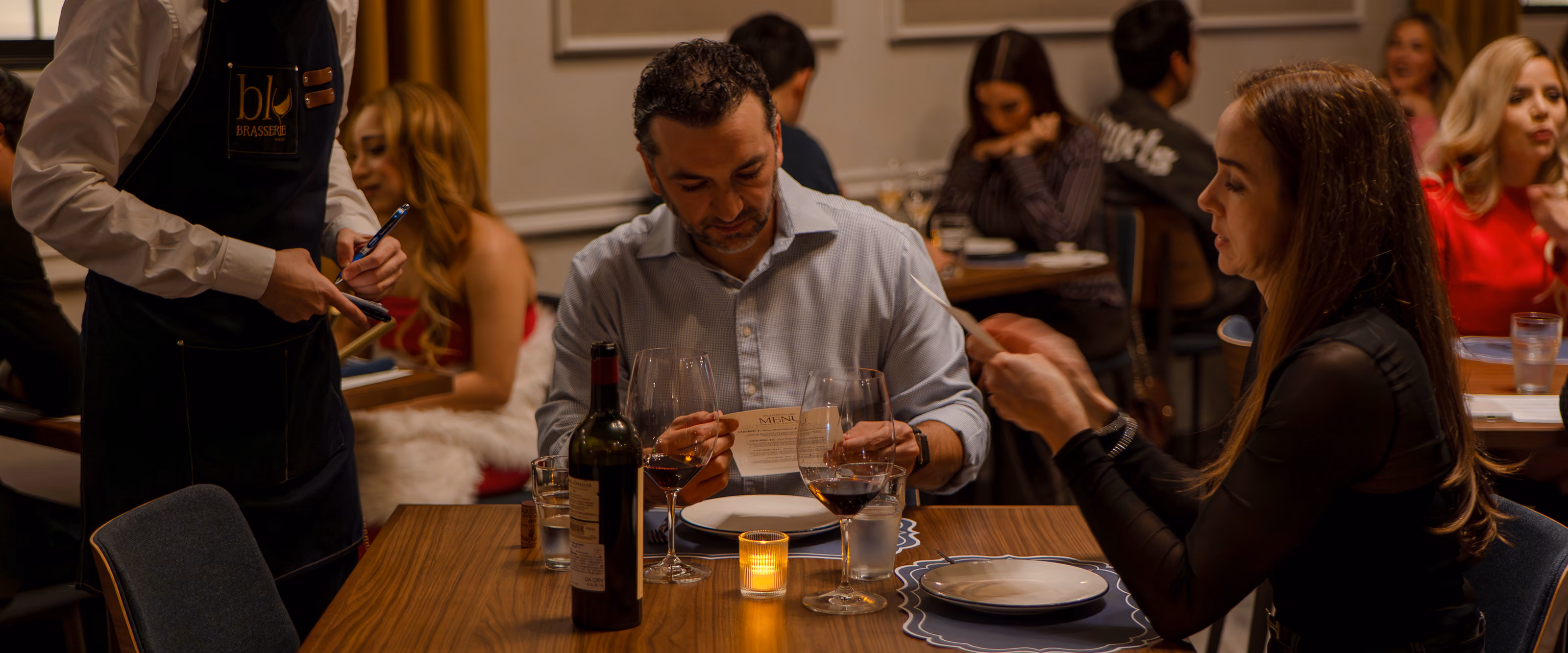 A server in a Blu Brasserie apron taking an order across a full dining room